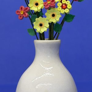 White ceramic vase with yellow punch and quilled flowers with tiny red roses and red quilled flowers.