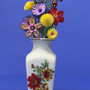 White ceramic vase with yellow, pink and blue, purple and turquoise, red and yellow and red flowers and leaves that are made from paper.